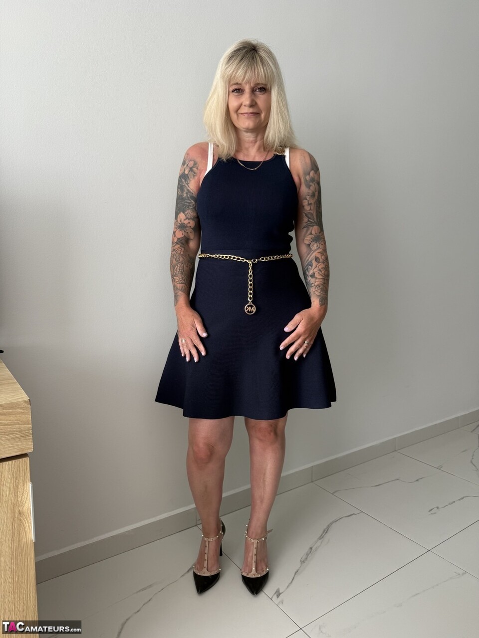 Tatuerad blond MILF klär av sig kjolen på högklackade skor